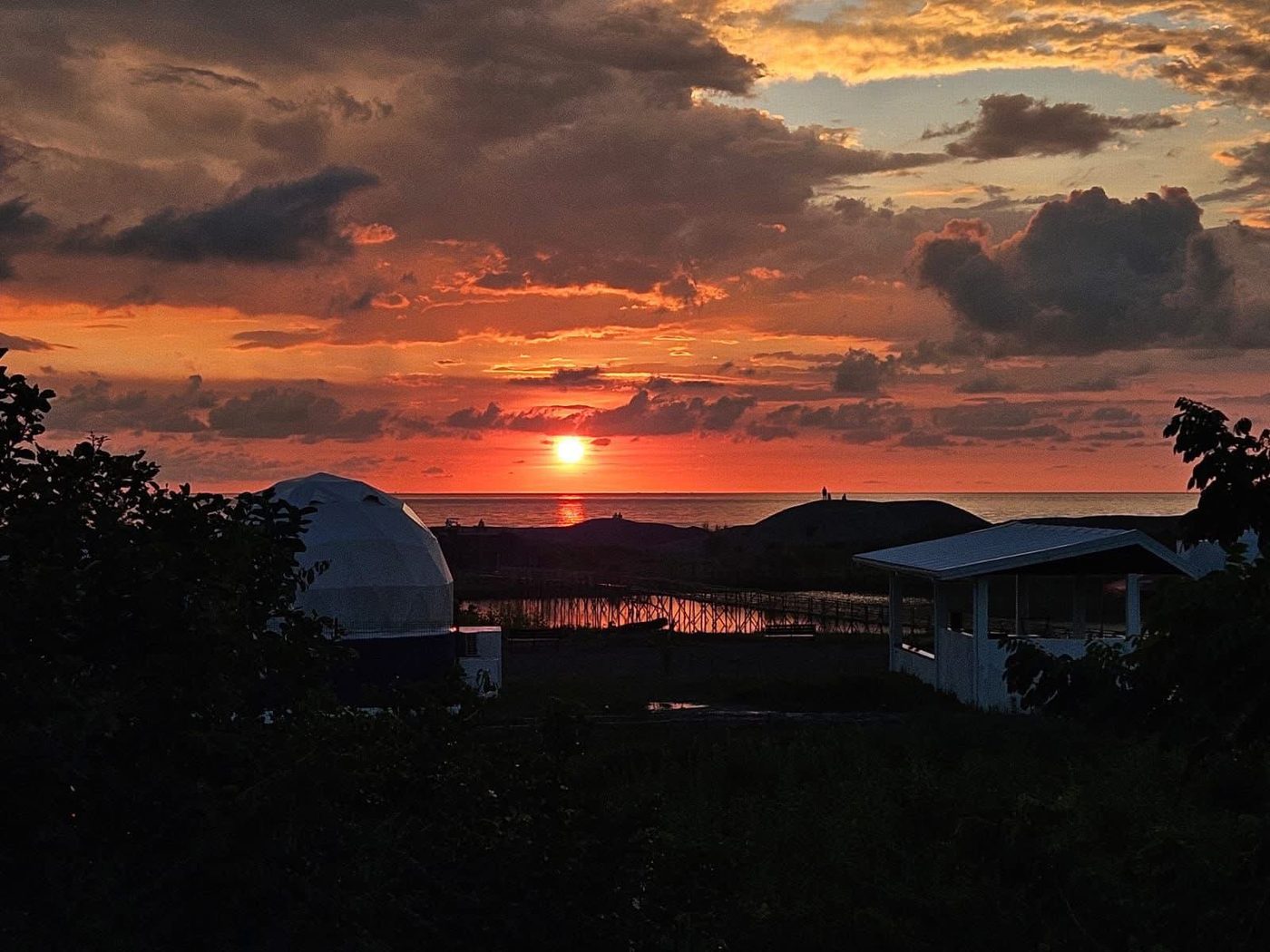 A Dome Pearl Villa silhouetted against a fiery sunset over the coast