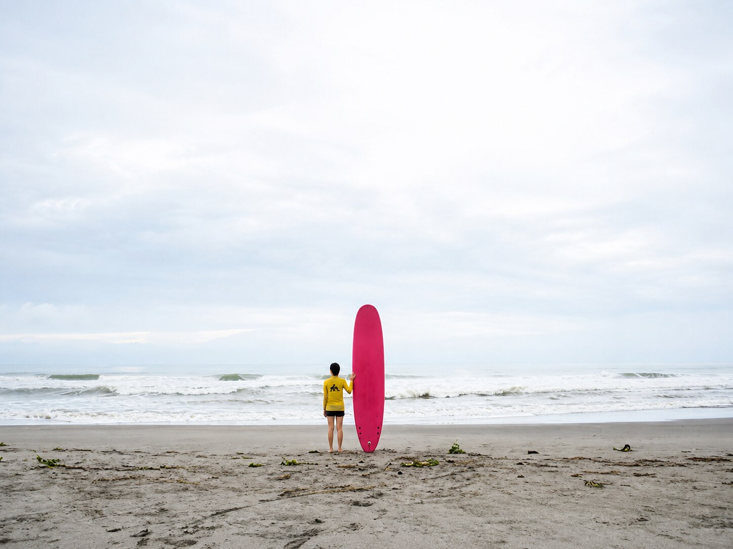 A surfer with a longboard facing the sea