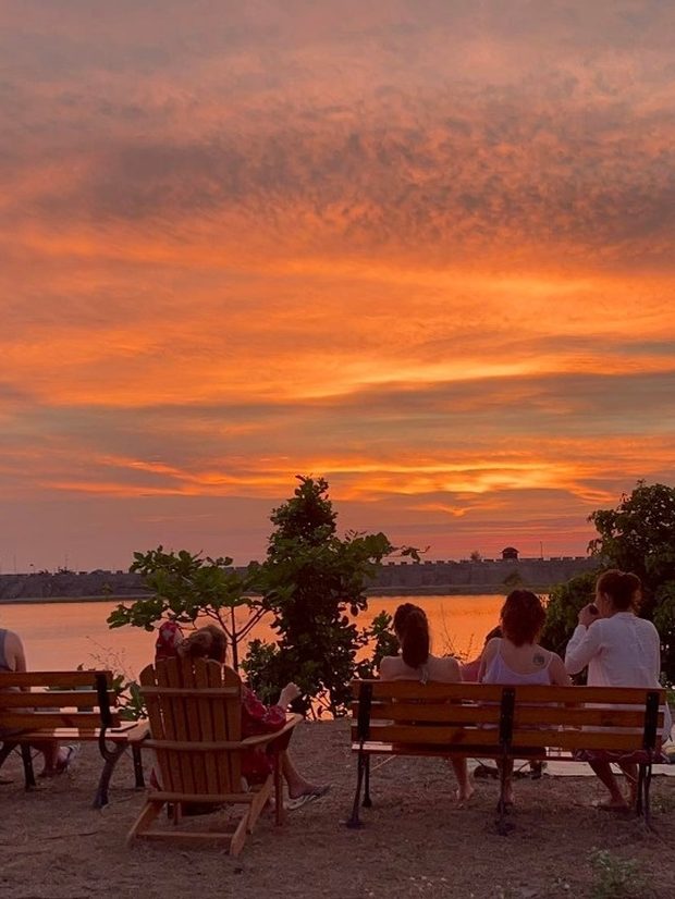 Guests watching a fiery sunset over the water from beach benches at AmanDagat