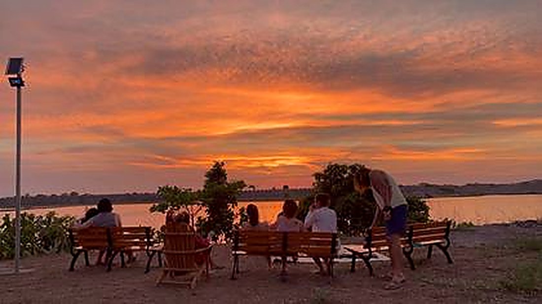 Guests watching a fiery sunset over the river from the benches
