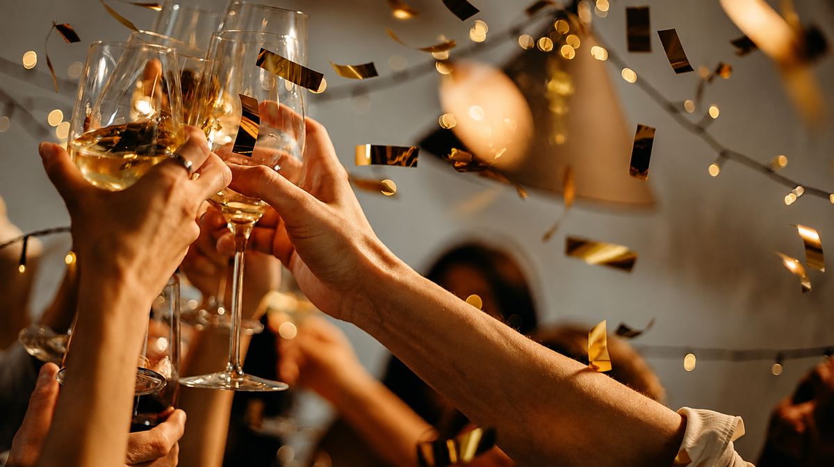 Glasses raised in a toast with golden confetti and string lights