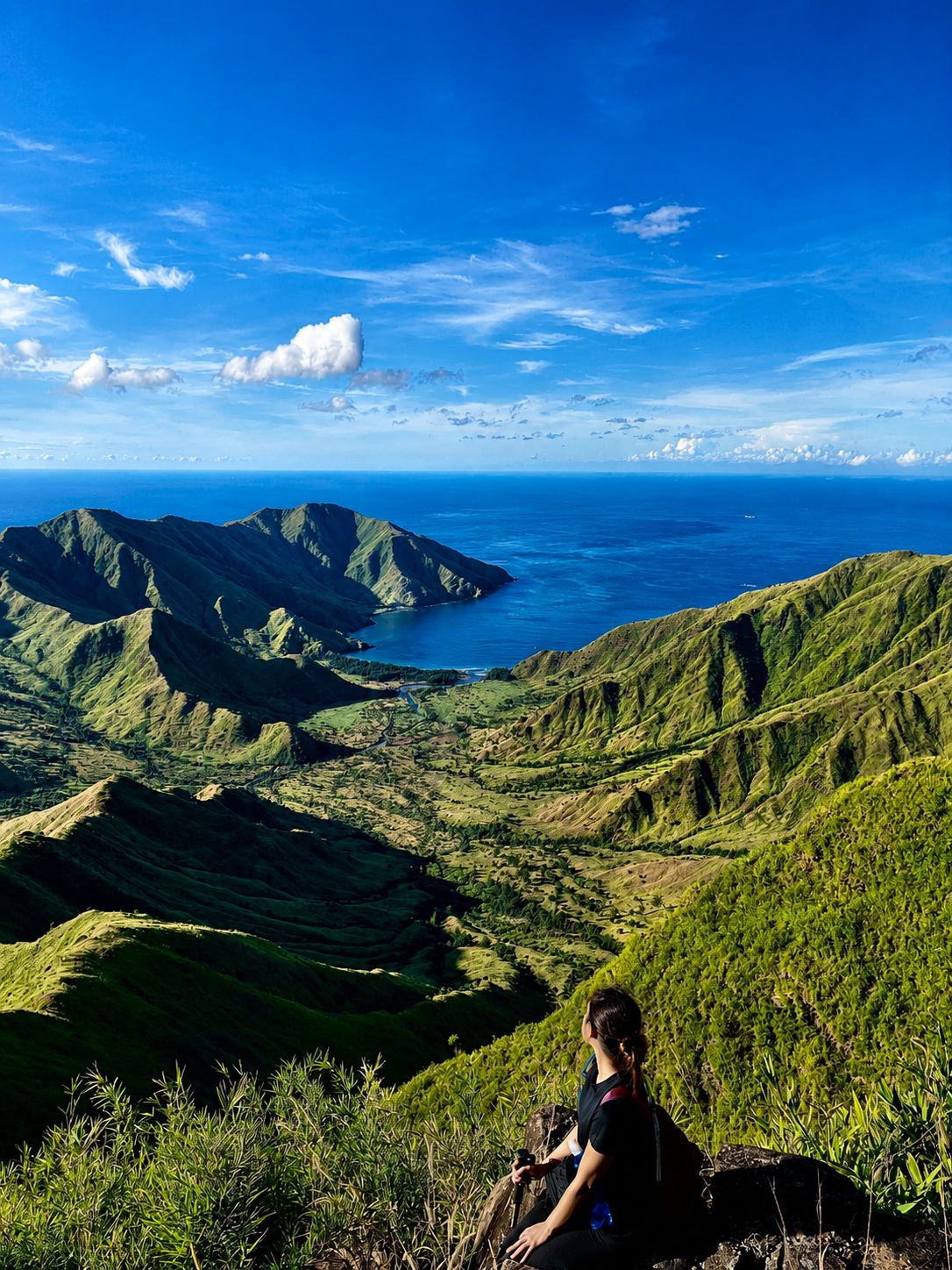 A hiker looking over green Zambales ridges down to a blue cove