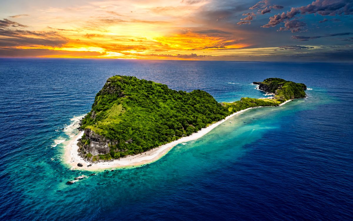 A lush green island ringed by white sand and turquoise water at sunset
