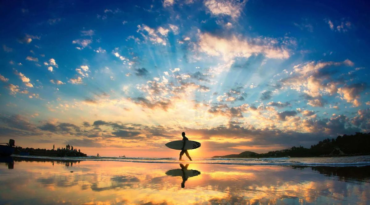 A surfer walking into a golden sunset at the water’s edge