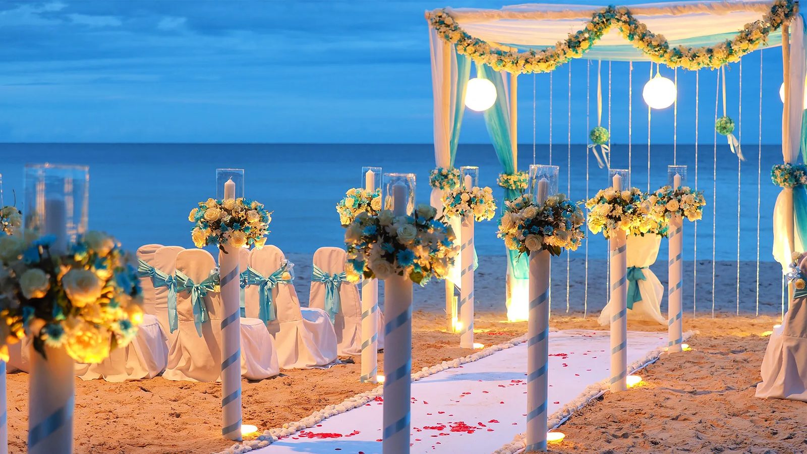 Candlelit beach wedding aisle and floral canopy in seafoam and white at dusk