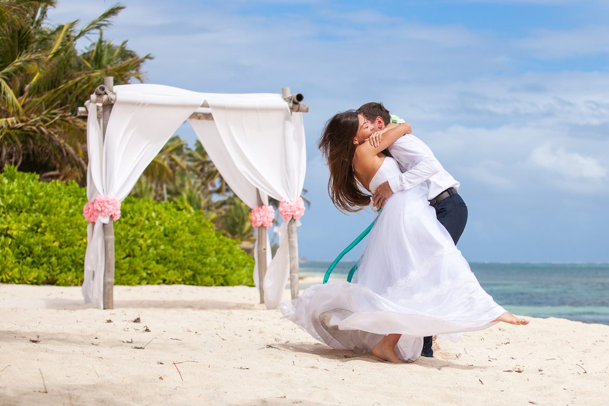 Newlyweds embracing beside a white ceremony arch on the beach