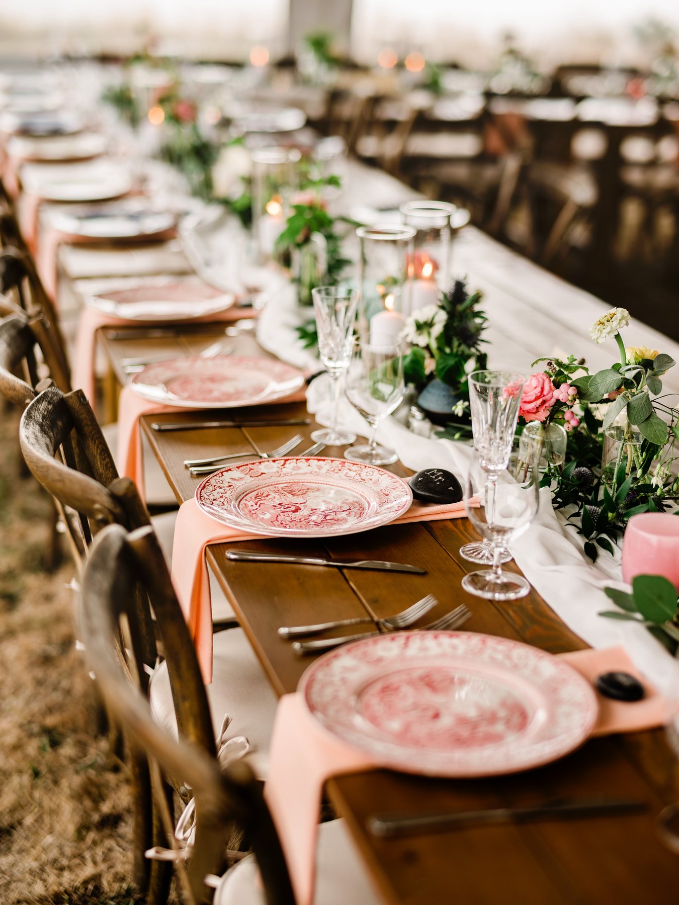 An elegant reception table set with patterned plates, blush napkins, candles and flowers