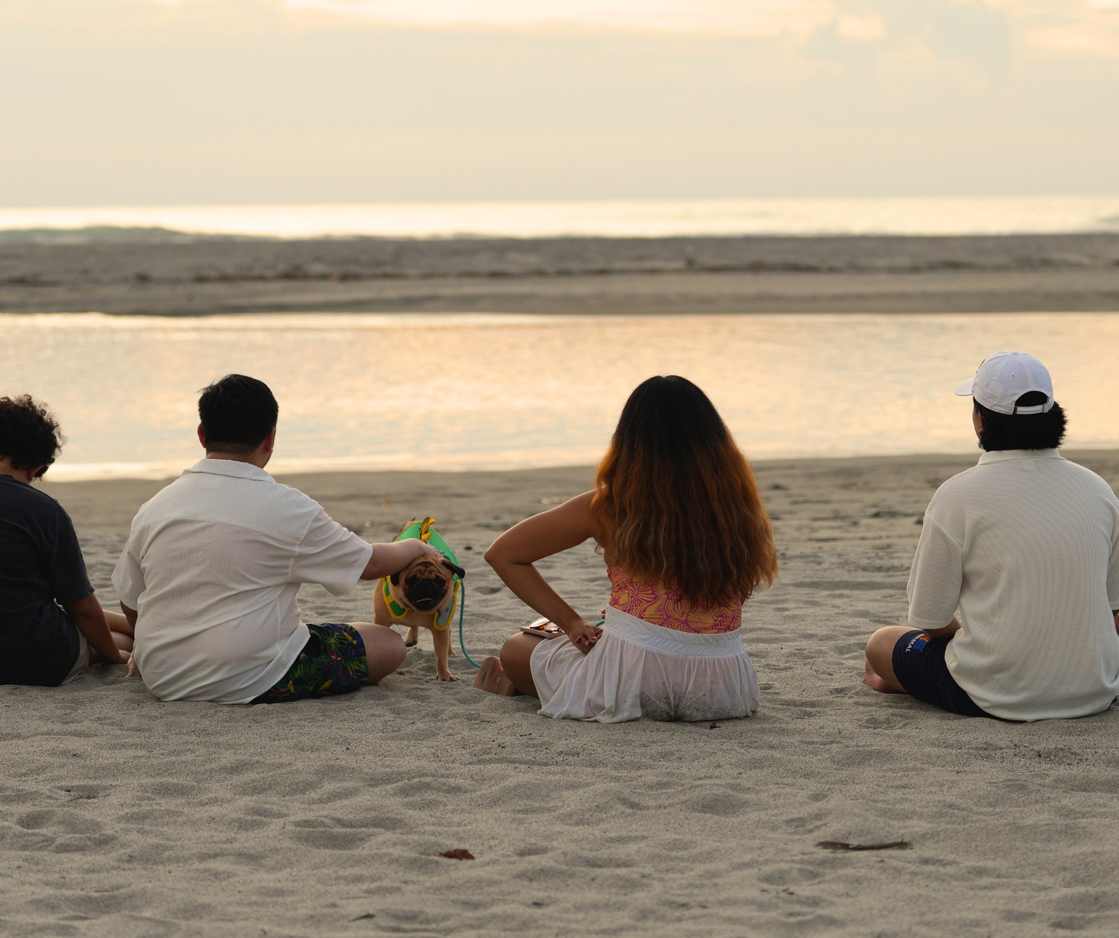 Friends and their pug watching the golden hour sea from the sand at AmanDagat