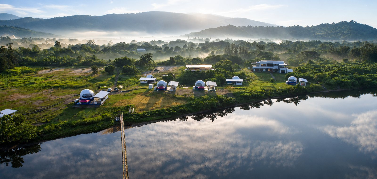 Aerial view of AmanDagat at sunrise &mdash; the Dome Pearl Villas beside the Sindol River, with the bridge and misty Zambales hills