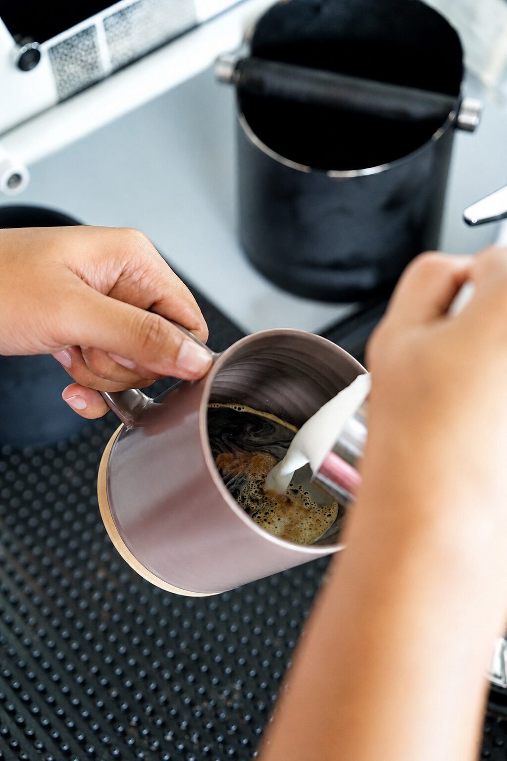 Barista pouring milk into freshly brewed coffee