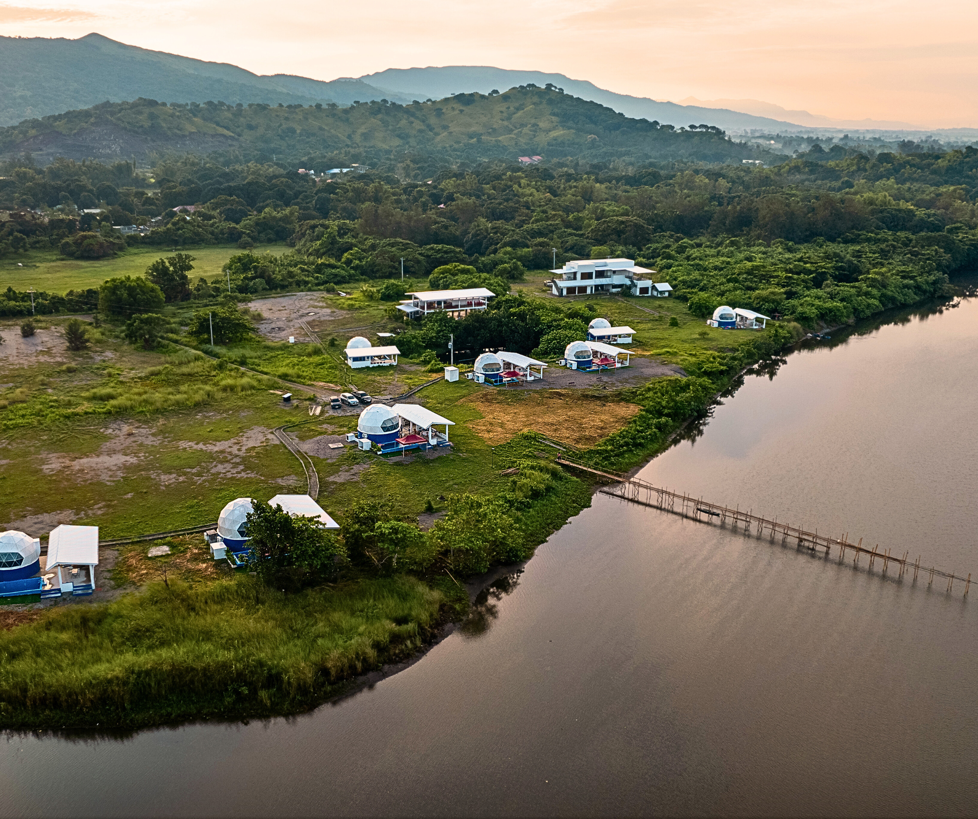Aerial view of AmanDagat's villas beside the river, with green hills beyond
