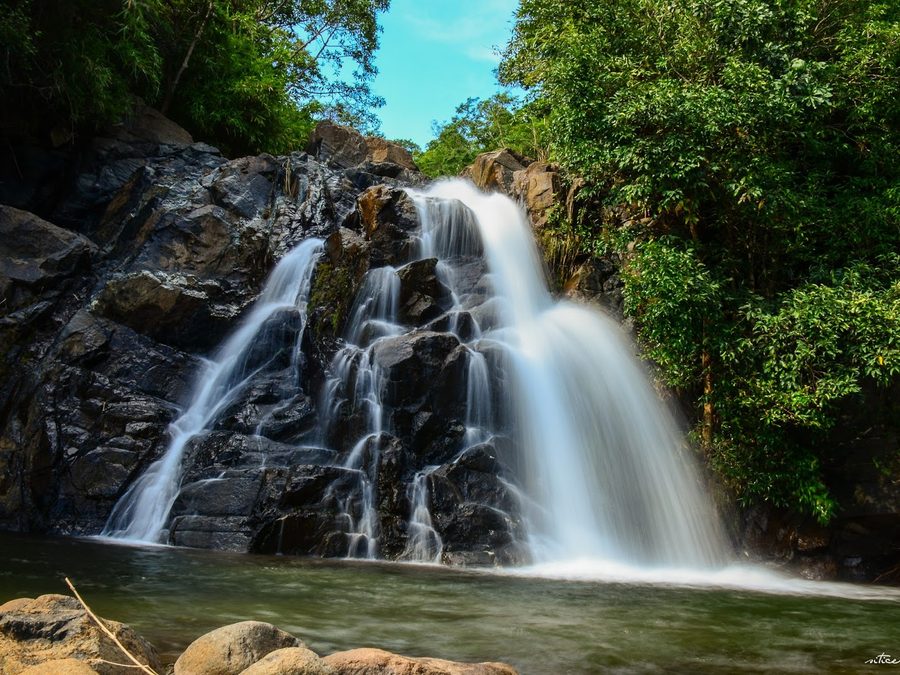 A wide waterfall cascading over dark rock into a natural pool